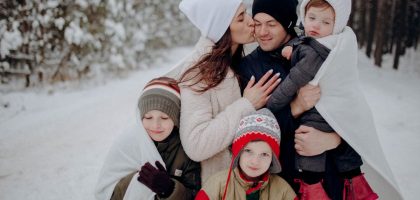 A joyful family enjoying a snowy day in a forest, wrapped in warm clothing.