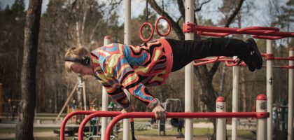 Young adult man exercises on outdoor gym bars in a colorful outfit in Vilnius, Lithuania.